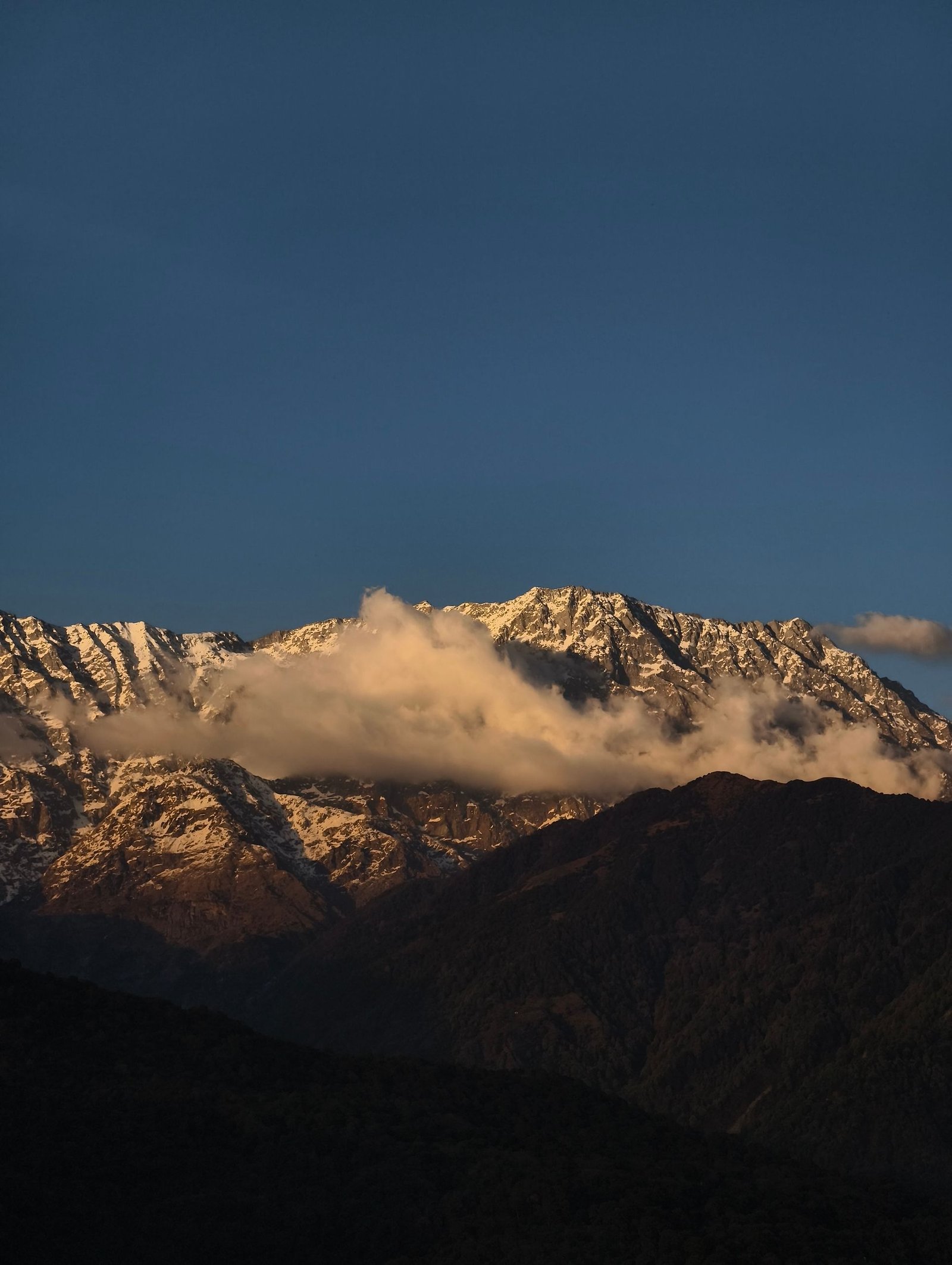 Breathtaking sunset view of the snow-capped Dhauladhar range in Dharamshala, India, with dramatic cloud formations.